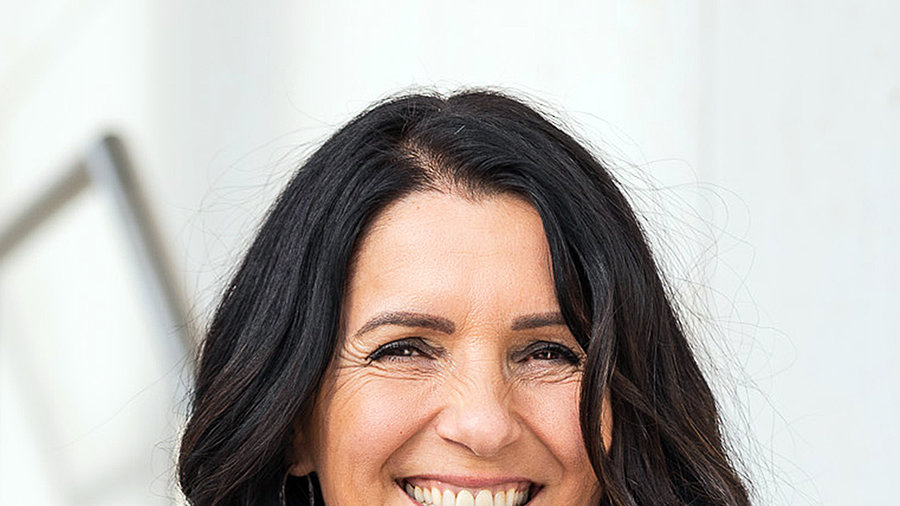 Professional portrait of a smiling woman with long dark hair wearing a patterned top and dark blazer.