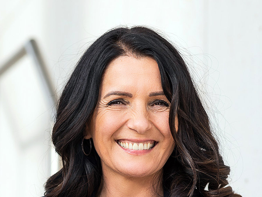 Professional portrait of a smiling woman with long dark hair wearing a patterned top and dark blazer.