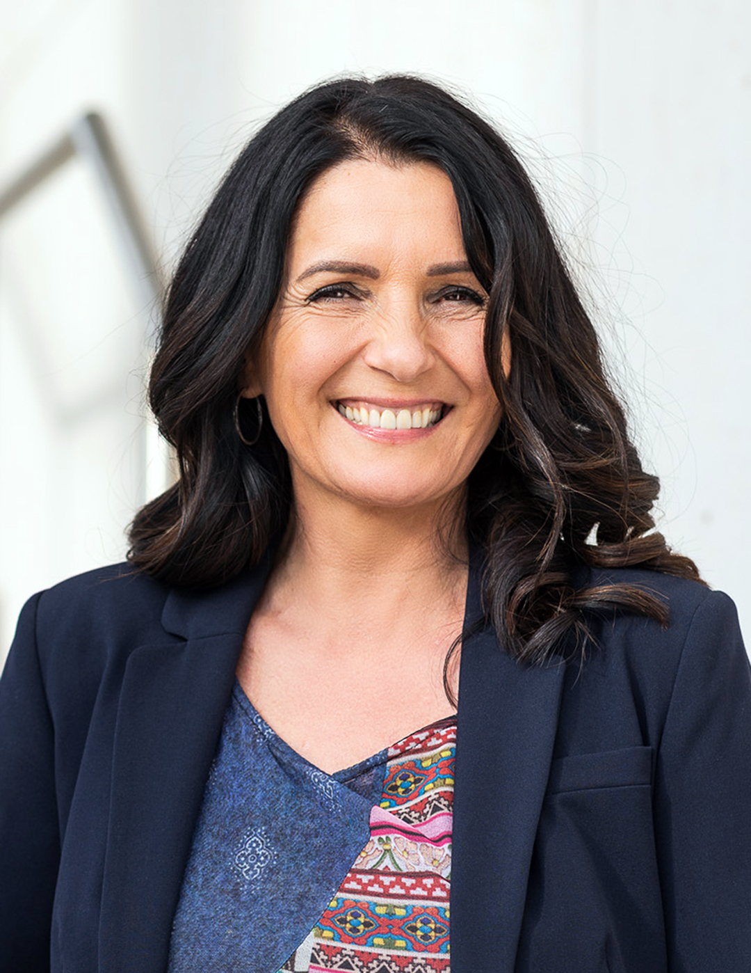 Professional portrait of a smiling woman with long dark hair wearing a patterned top and dark blazer.